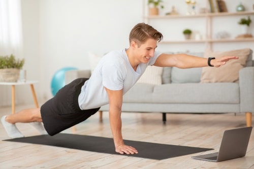 junger Mann beim Online Personal Training junger Mann trainiert auf Matte vor seinem Laptop