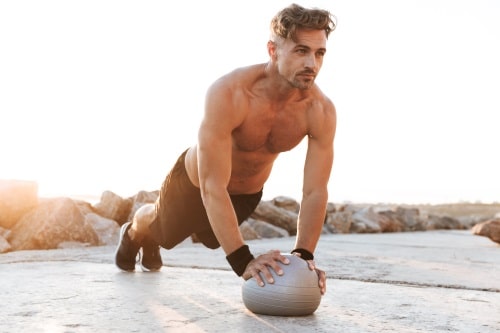 Mann beim Outdoor-Training mit Personal Trainer Mann oberkörperfrei trainiert mit Ball beim Personal Training