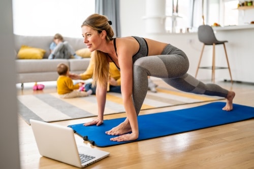 Unternehmerin beim Online Personal Training mit Farris Elghadi Frau trainiert auf Matte vor ihrem Laptop, im Hintergrund sind Kinder